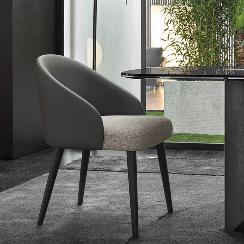 NOTI Chair positioned next to a dining table on a gray carpet, black metal legs, dark gray leather backrest, light gray fabric seat.