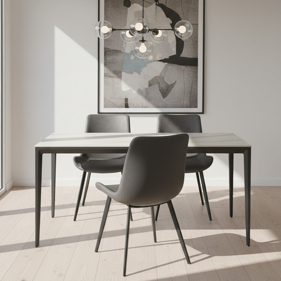 RAG Contemporary Sintered Stone Dining Table in a modern dining room. The table features a white marble-look top and a dark gray aluminum base, paired with dark gray chairs. Natural light shines in from the left.