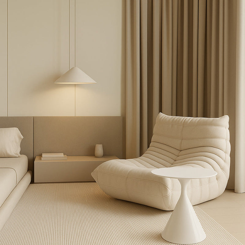 Togo-style cream fabric lounge chair in a minimalist bedroom setting with soft warm lighting and a white side table.