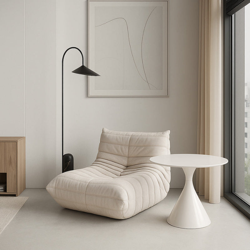 Iconic Togo-style caterpillar lounge chair in light beige textile, styled with a sleek black floor lamp and minimalist wall art.