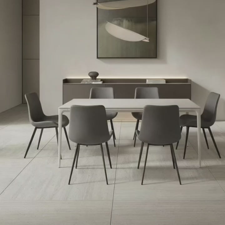 Contemporary Dining Table with a white top and white aluminum base, set in a bright, all-white modern dining area. The table is surrounded by six grey dining chairs with dark legs.