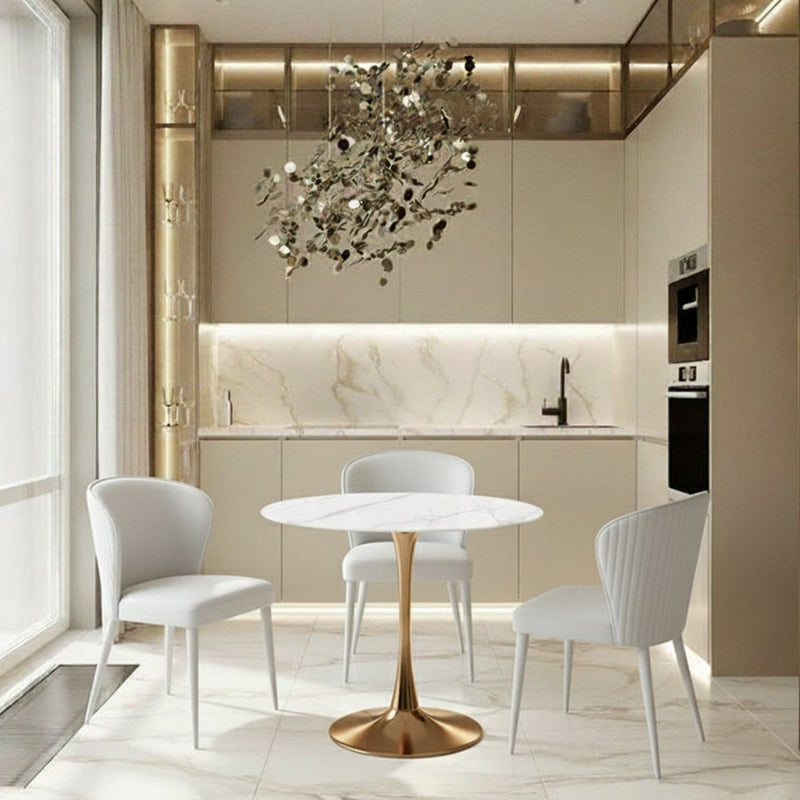 Bright kitchen scene showcasing the TULIP 90CM Round Table with a Snow Mountain White ceramic top and a champagne gold base, set with contemporary white leather dining chairs.