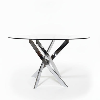 45-degree angled view of the VERDIS round glass dining table featuring a clear tempered glass top and mirror-finish stainless-steel legs